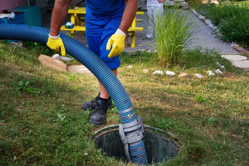 Technician feeding a pumping hose into an open septic access lid in a lawn
