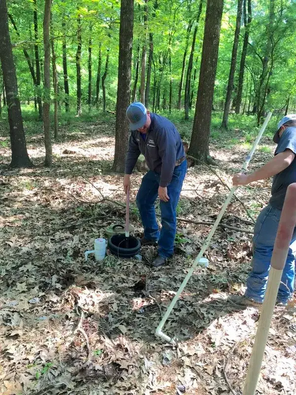 Crew locating and probing a septic system in a wooded lot