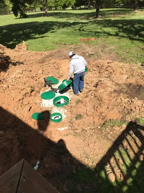 Worker finishing a multi-chamber septic installation with green riser lids