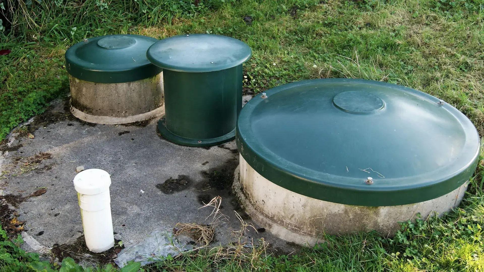 Three green septic tank risers at ground level in a yard